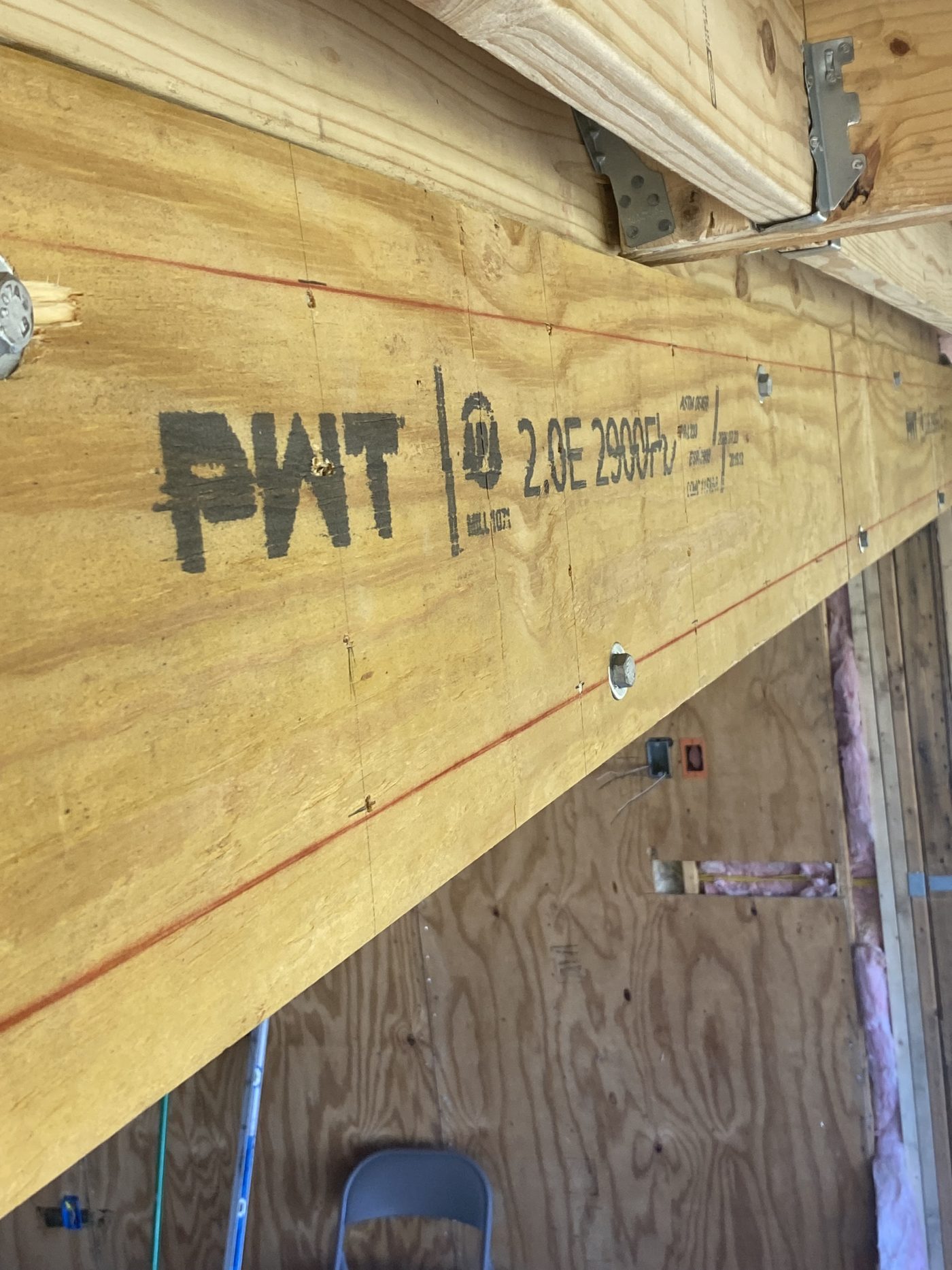Face of a multi-ply beam with through-bolt heads and washers in two staggered rows along the span, bearing on a post at the end
