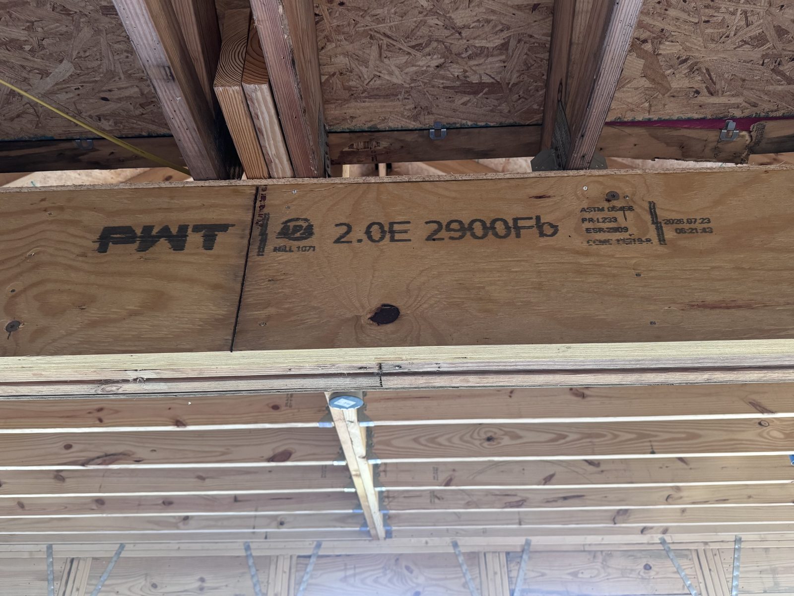Underside of a multi-ply beam showing one LVL ply with even veneer lines next to sawn lumber plies with knots and checking