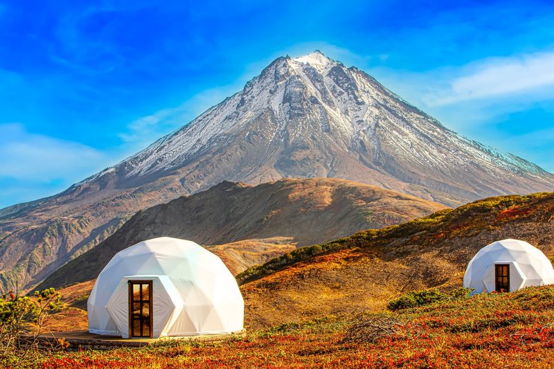 Two white geodesic dome homes on a hillside below a snow-capped mountain