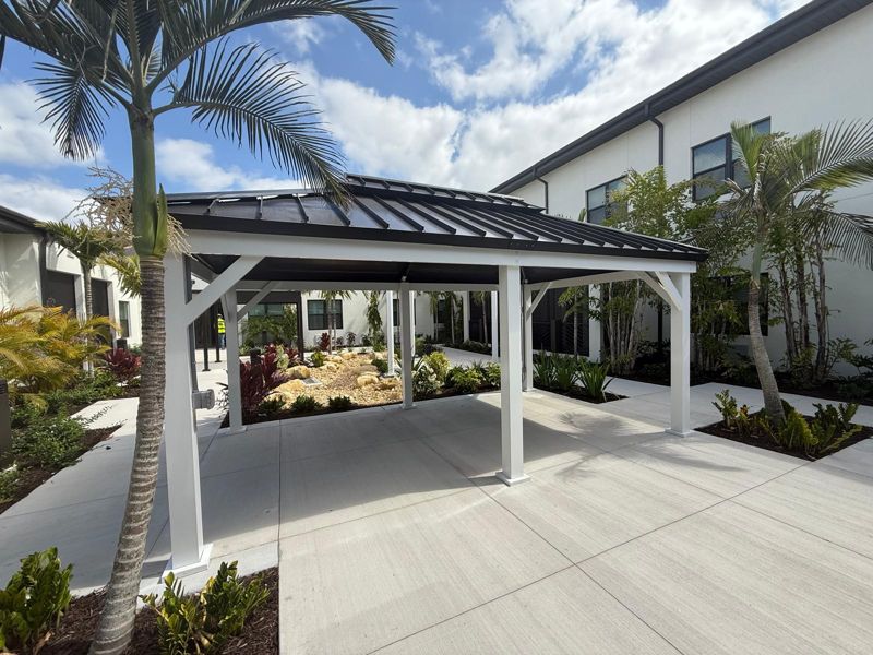 White hip-roof metal canopy in a landscaped courtyard in Naples, Florida